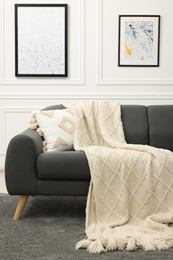 Photo of Comfortable sofa with beige blanket and pillow in living room