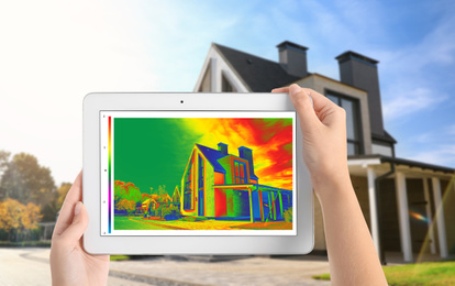 Image of Woman detecting heat loss in house using thermal viewer on tablet, outdoors. Energy efficiency