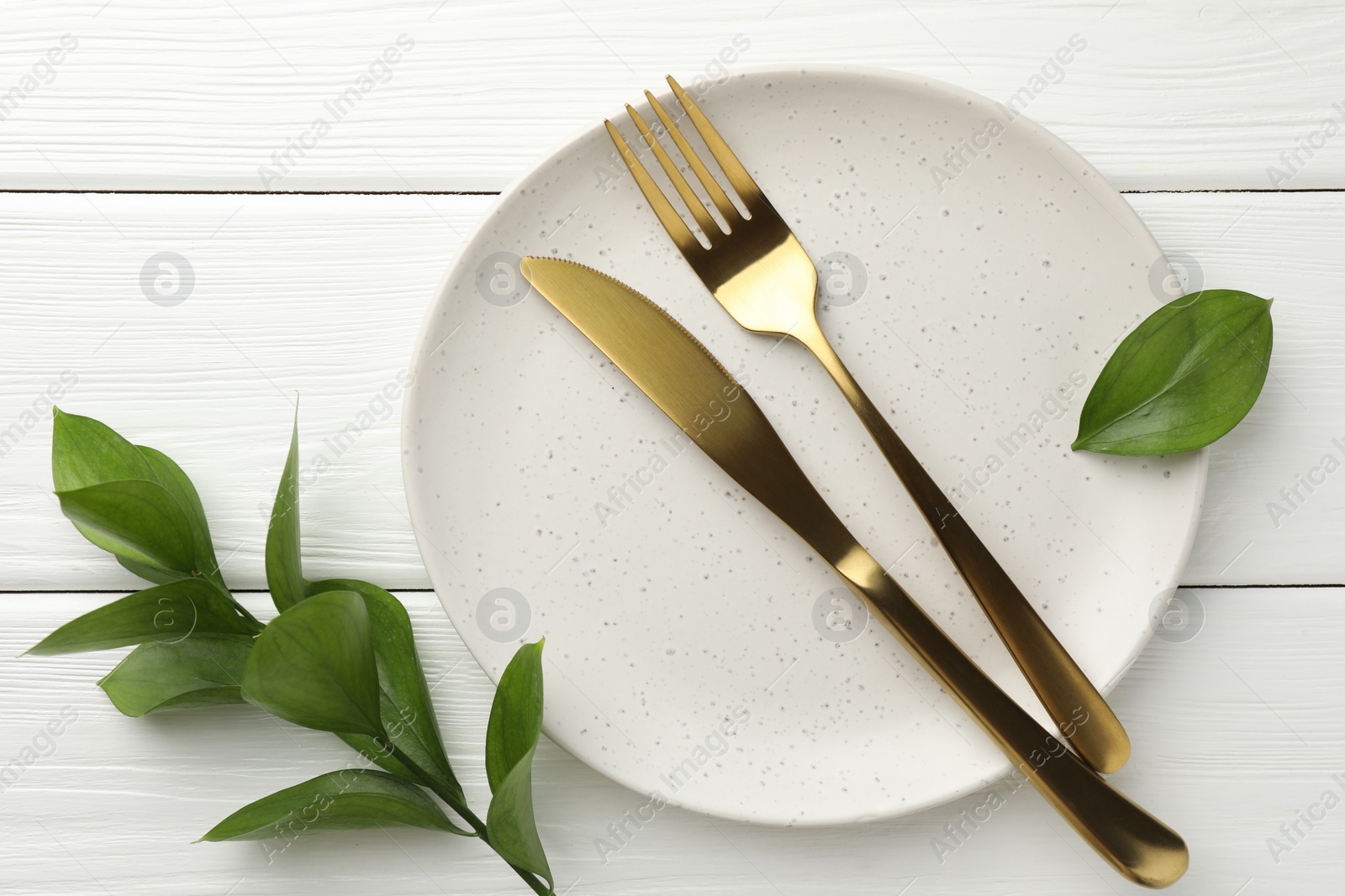 Photo of Stylish setting with cutlery, green leaves and plate on white wooden table, flat lay