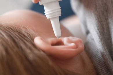 Mother dripping medication into daughter's ear on blurred background, closeup