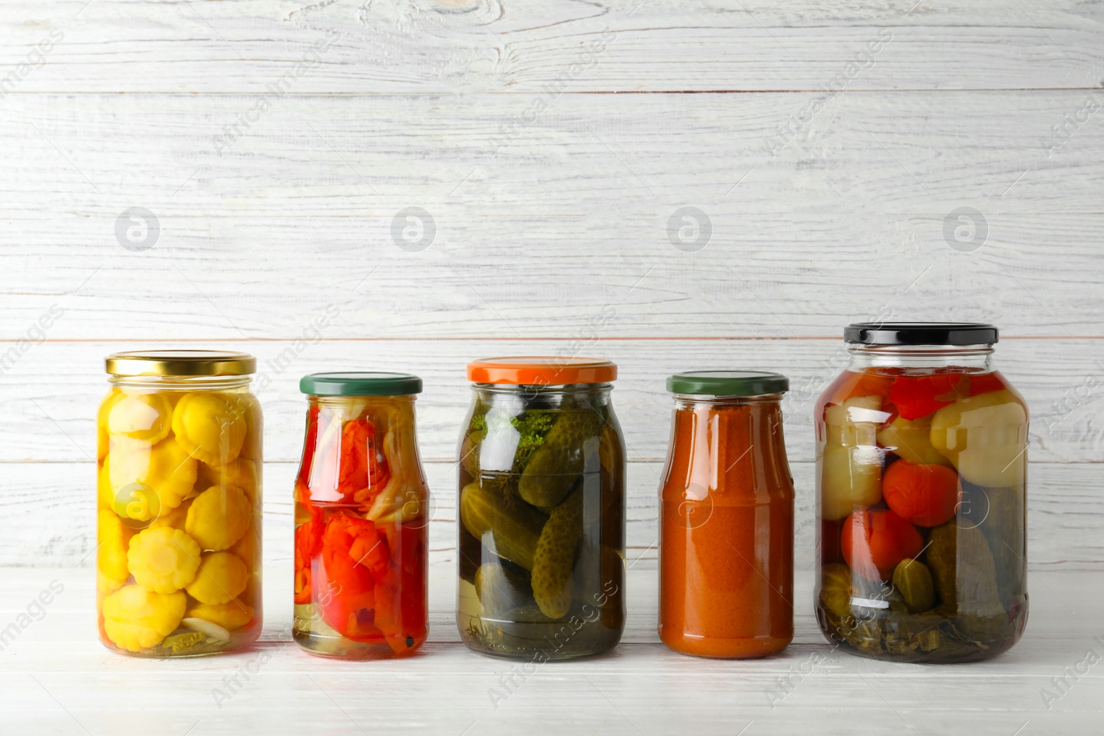 Photo of Jars with pickled vegetables on white table against wooden background