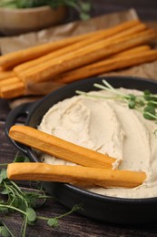 Delicious hummus with grissini sticks and ingredients on wooden table, closeup