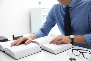 Photo of Notary studying law books at table in office, closeup