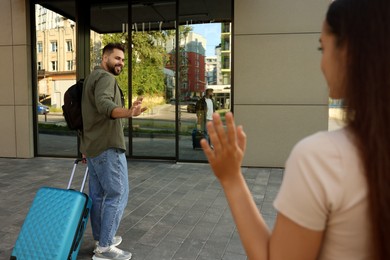 Photo of Long-distance relationship. Woman waving to her boyfriend with luggage outdoors, selective focus