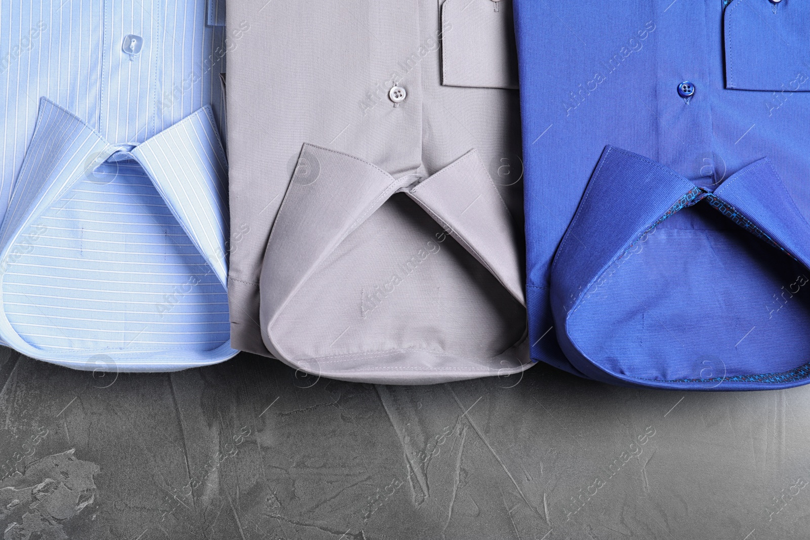 Photo of Stylish folded shirts on grey stone table, flat lay. Dry-cleaning service