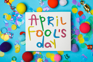 Paper note with phrase APRIL FOOL'S DAY and decor on light blue background, flat lay