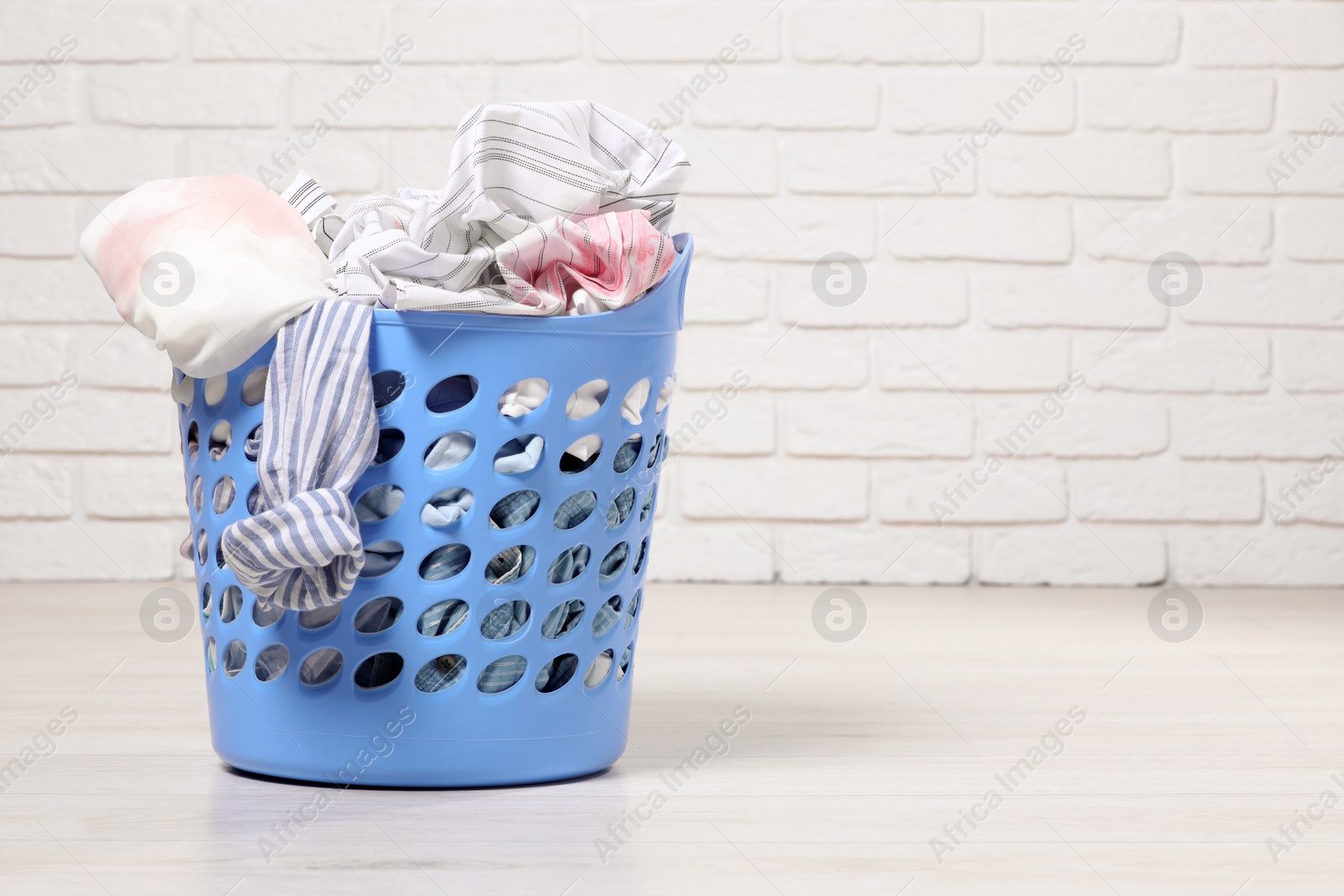 Photo of Laundry basket with clothes near white brick wall. Space for text