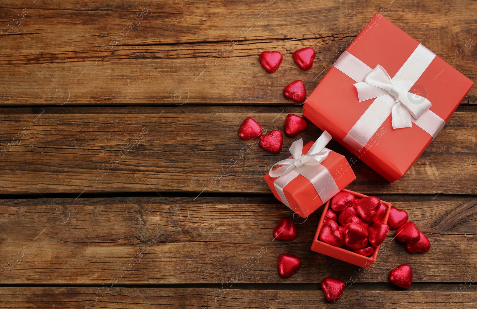 Photo of Heart shaped chocolate candies and gift boxes on wooden table, flat lay. Space for text