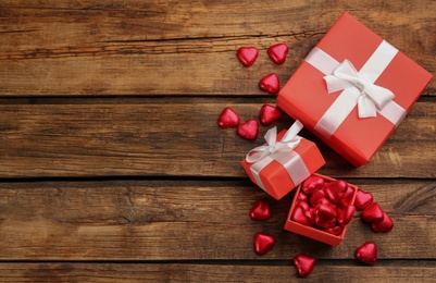 Photo of Heart shaped chocolate candies and gift boxes on wooden table, flat lay. Space for text