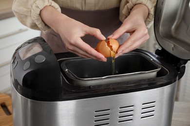 Photo of Making dough. Woman breaking egg into breadmaker pan, closeup