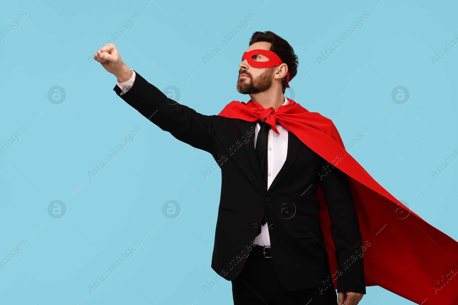 Photo of Businessman wearing red superhero cape and mask on light blue background