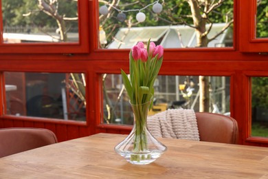 Photo of Pink tulips in glass vase on wooden table at terrace