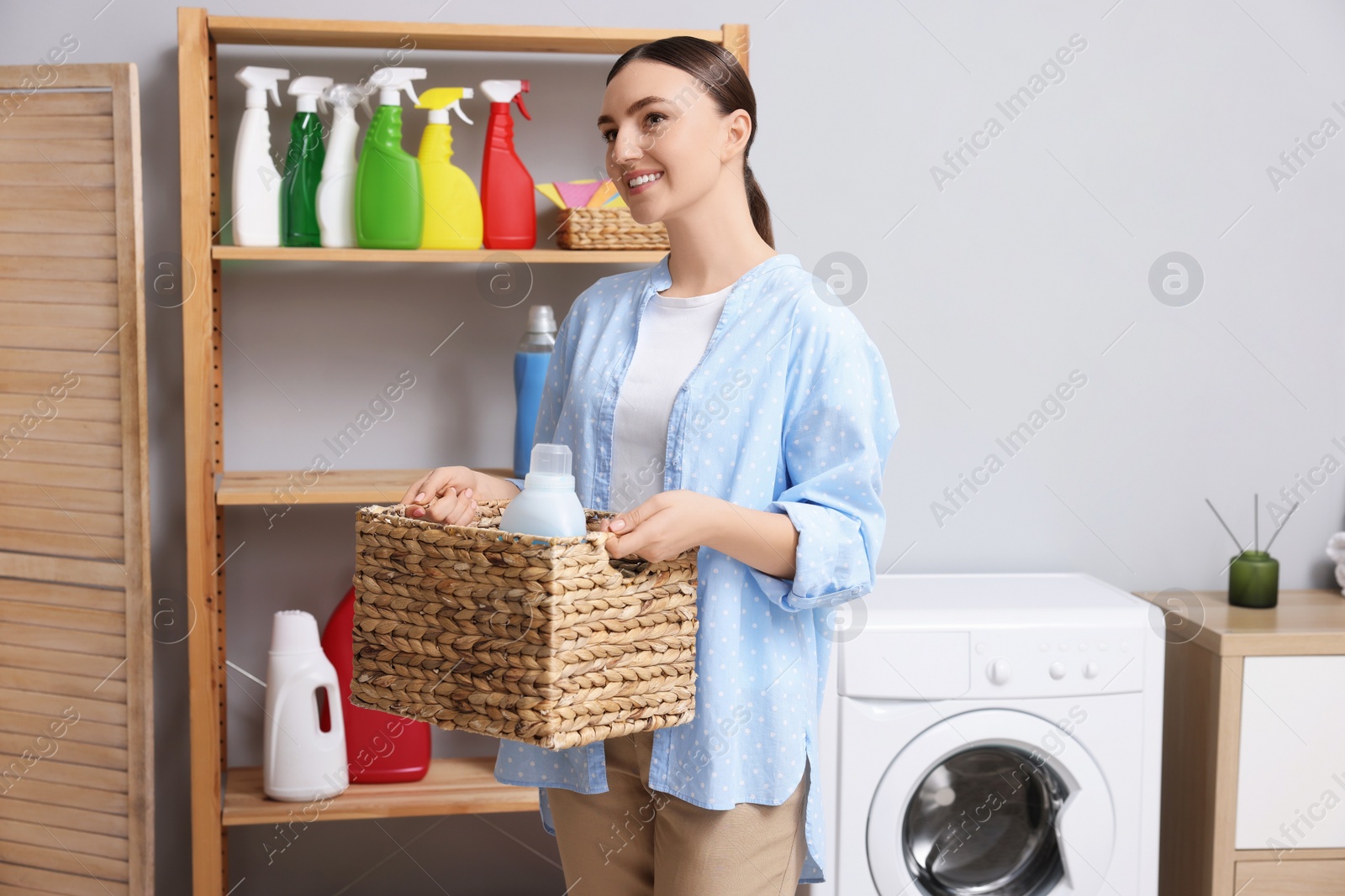 Photo of Woman holding wicker basket with detergent in laundry room