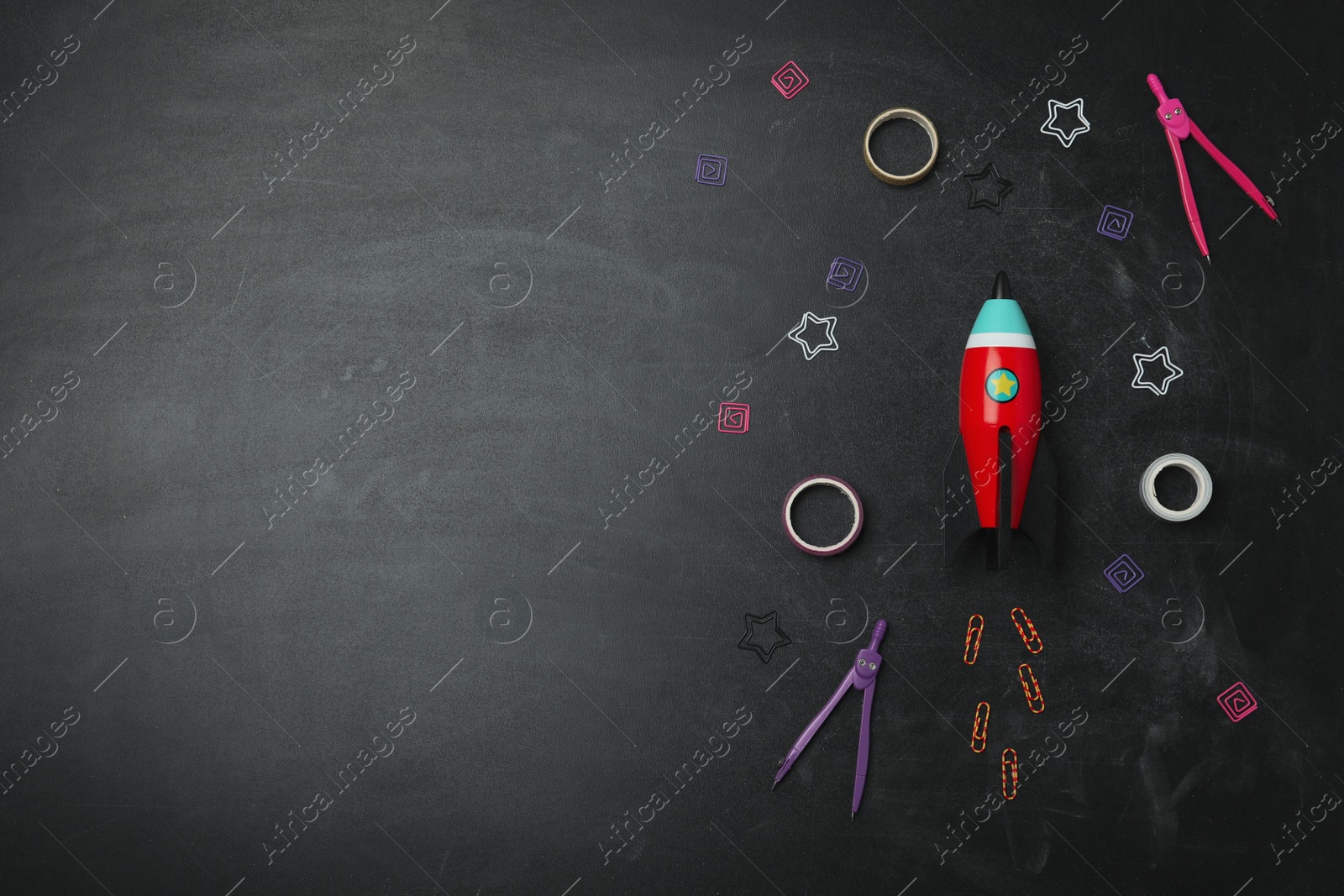 Photo of Bright toy rocket and school supplies on chalkboard, flat lay. Space for text