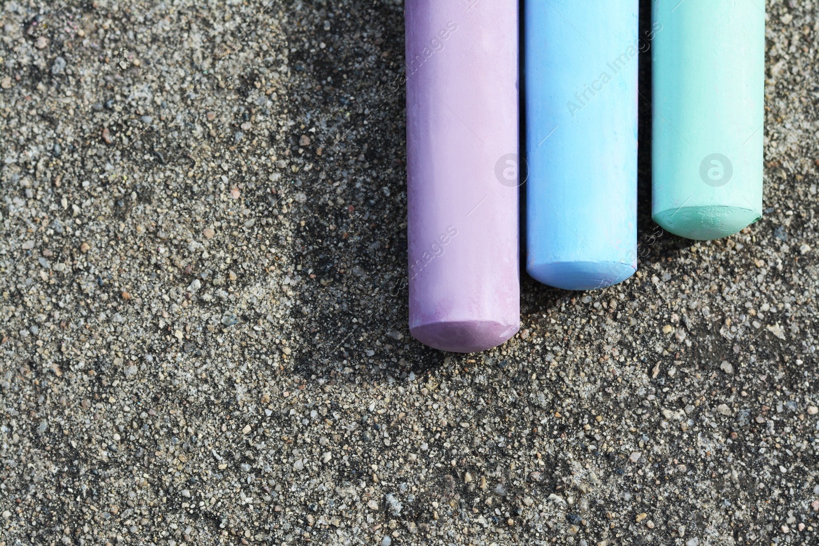 Photo of Colorful chalk sticks on asphalt, flat lay. Space for text