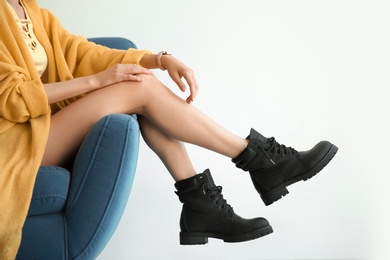 Young woman with sexy legs in armchair on light background