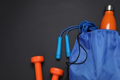 Photo of Blue drawstring bag, thermo bottle, skipping rope and dumbbells on black background, flat lay. Space for text