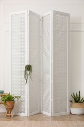 Folding screen and beautiful houseplants near white wall in room. Interior design