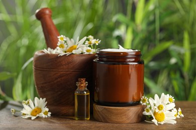 Photo of Jar of hand cream, chamomiles and cosmetic product on wooden table