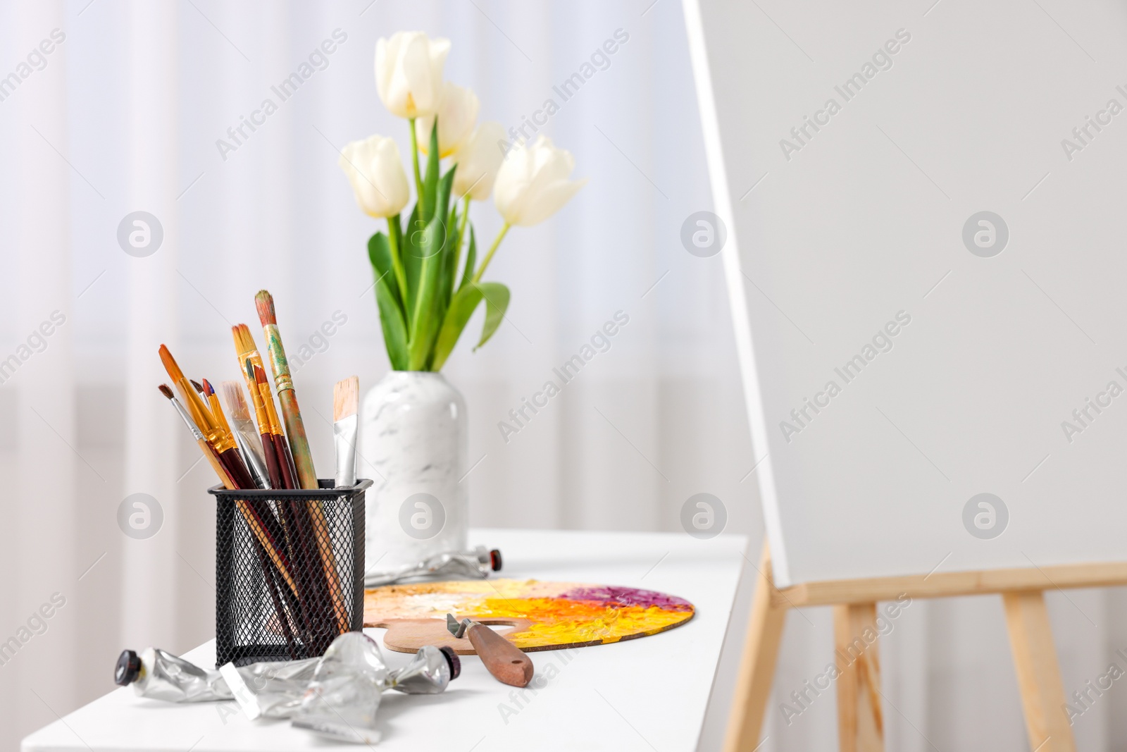 Photo of Wooden easel with canvas and art supplies on table indoors. Space for text