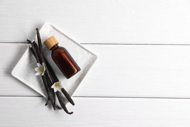 Photo of Vanilla pods, essential oil and flowers on white wooden table, top view. Space for text