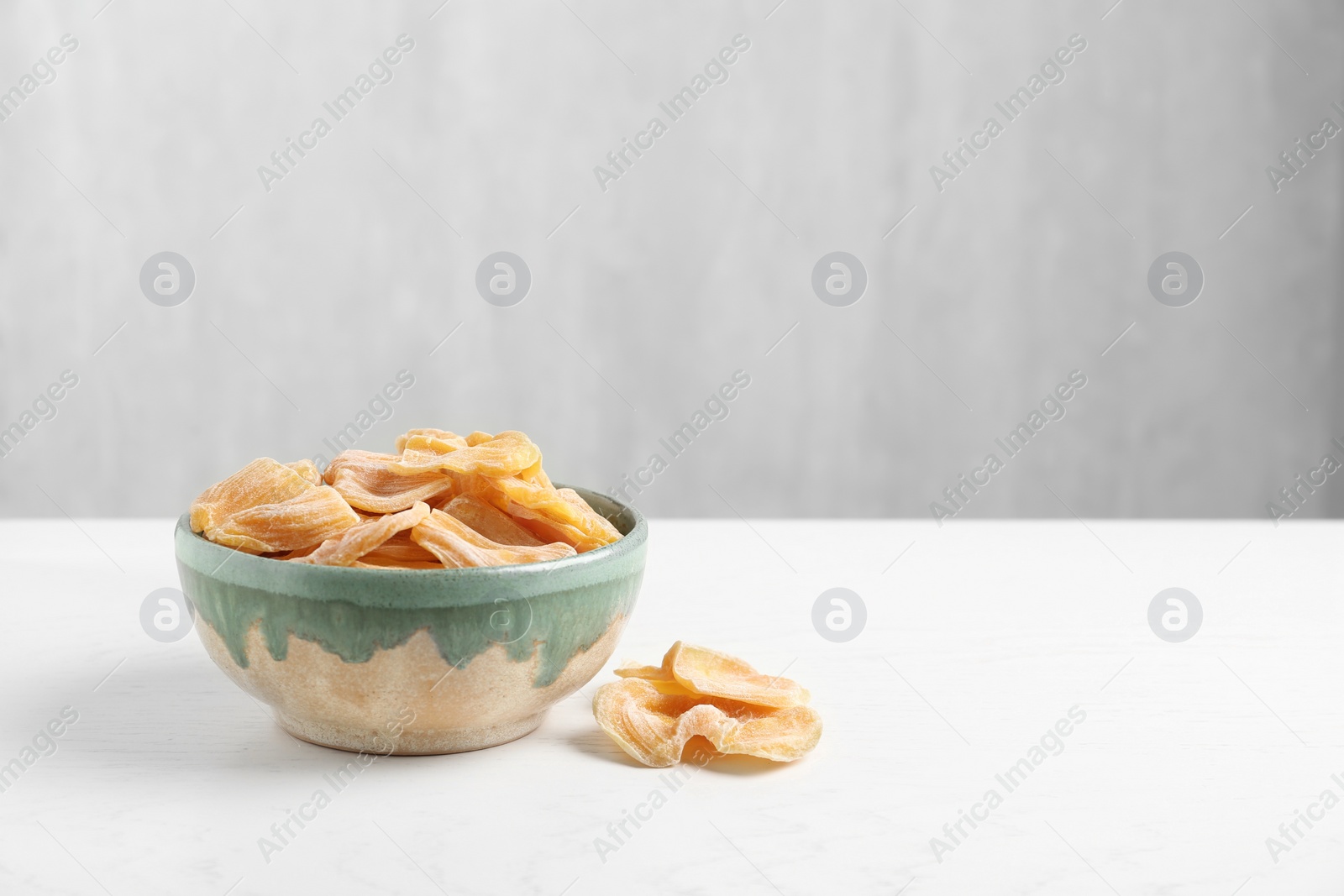 Photo of Delicious dried jackfruit slices in bowl on white wooden table. Space for text