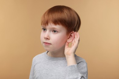 Photo of Little boy with hearing problem on pale brown background