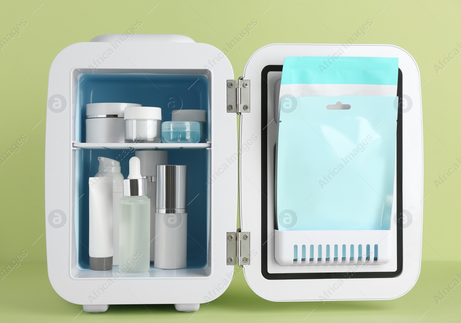 Photo of Open cosmetic refrigerator with skin care products on light green background