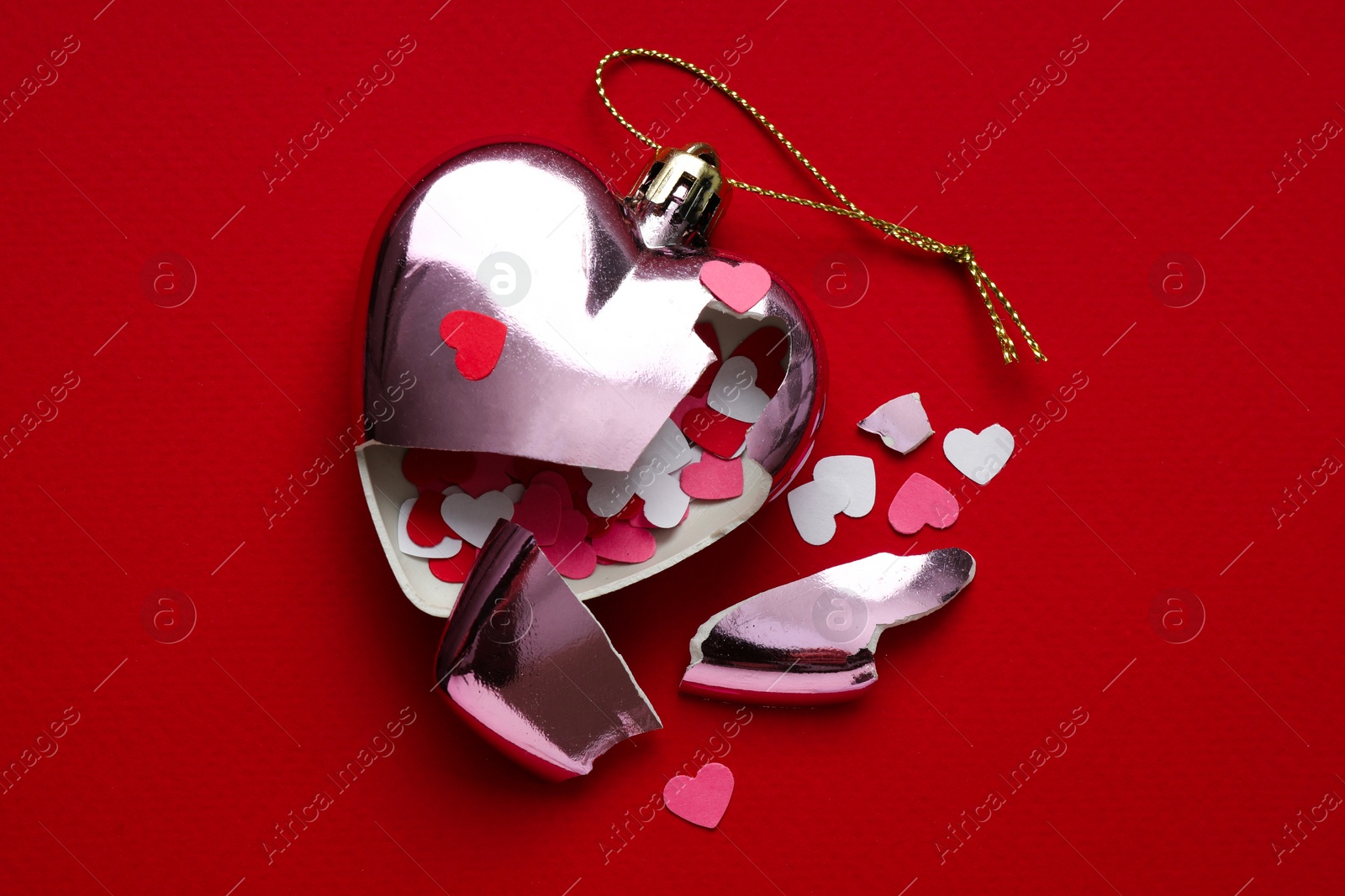 Photo of Crashed bauble in shape of heart with confetti on red background, top view. Broken heart