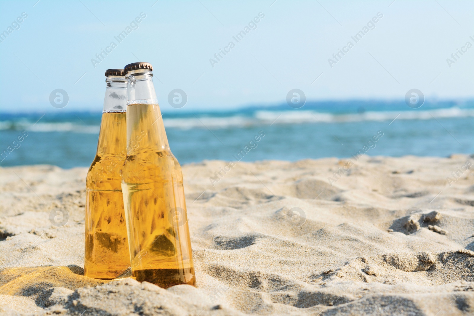 Photo of Bottles of cold beer on sandy beach near sea, space for text