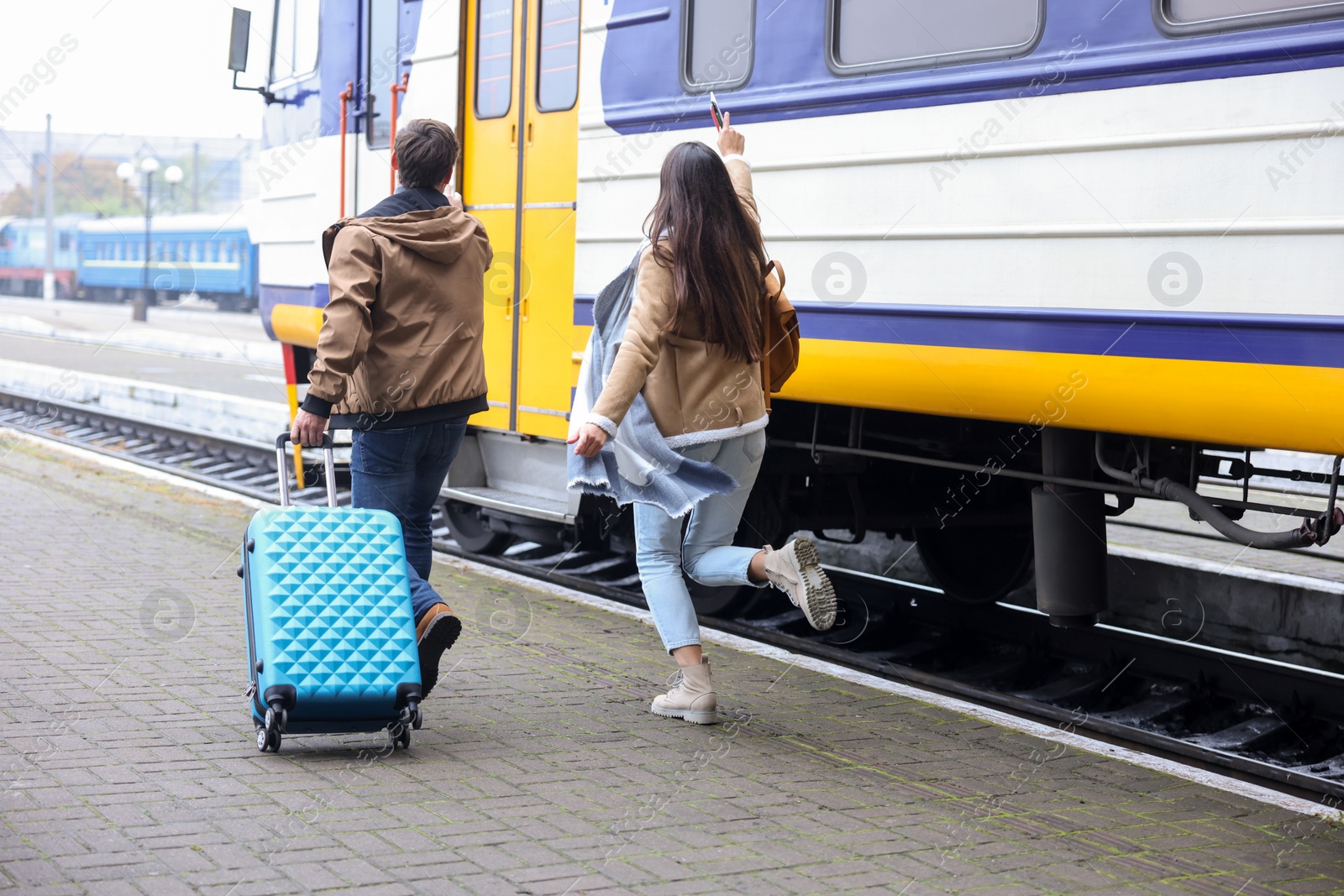 Photo of Being late. Couple with suitcase running towards train at station, back view. Space for text