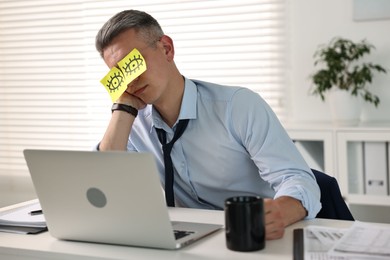 Photo of Man with fake eyes painted on sticky notes snoozing at workplace in office