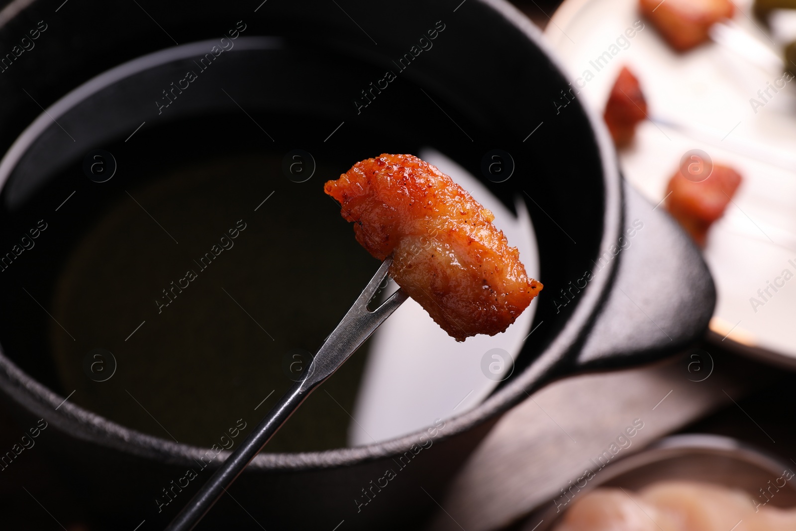 Photo of Fondue pot and fork with fried meat piece on wooden table, closeup