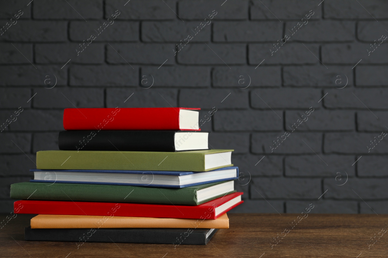 Photo of Stack of hardcover books on wooden table near dark brick wall, space for text