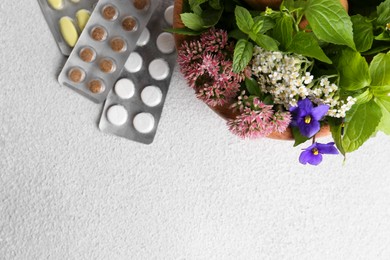 Wooden mortar with fresh herbs, flowers and pills on white table, top view. Space for text