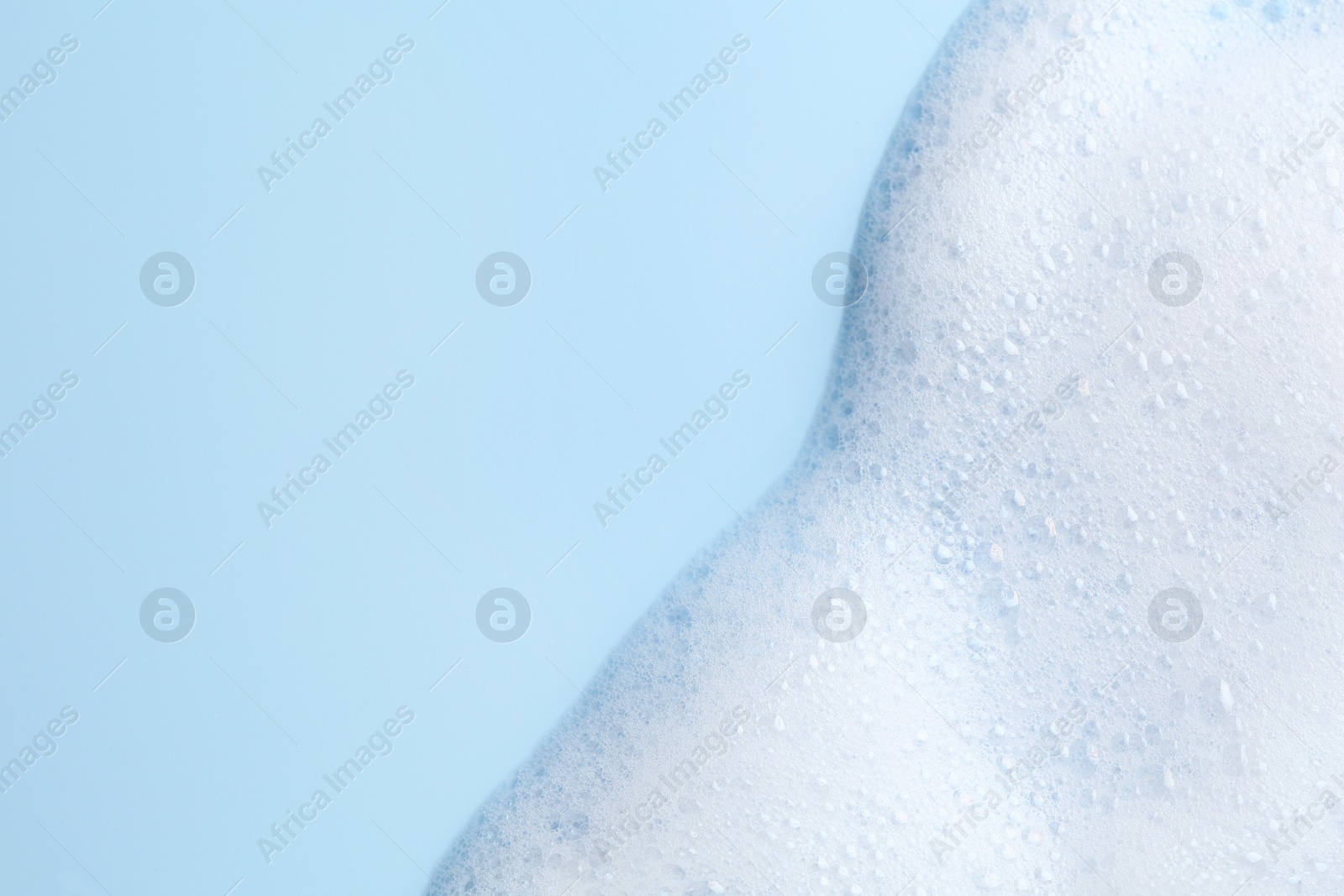 Photo of White fluffy foam on light blue background, top view. Space for text