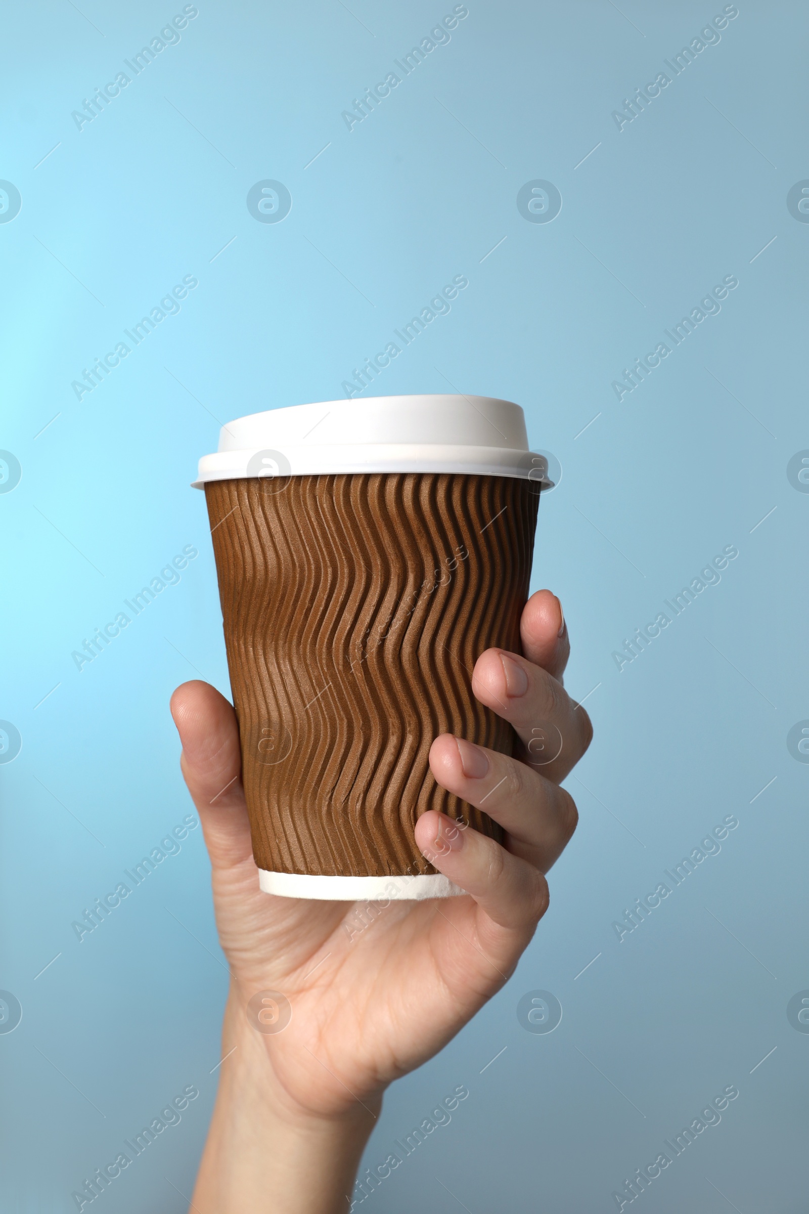 Photo of Woman holding takeaway paper coffee cup on blue background, closeup