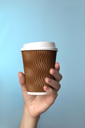 Woman holding takeaway paper coffee cup on blue background, closeup