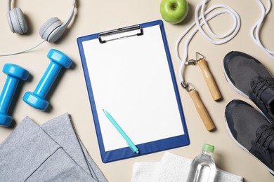 Photo of Clipboard with paper sheet, pen and sports equipment on beige table, flat lay. Personal training
