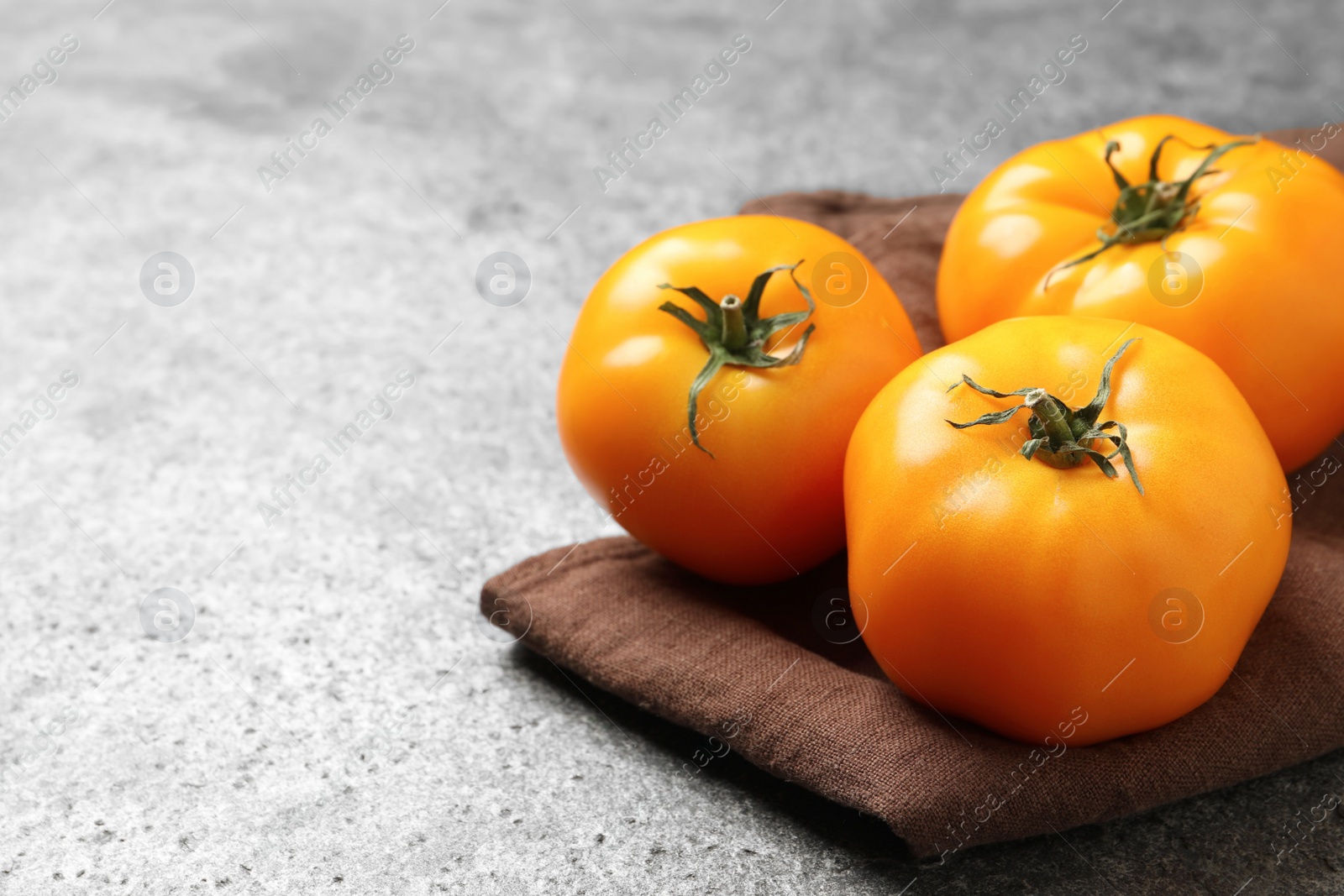 Photo of Fresh ripe yellow tomatoes on grey table, closeup. Space for text