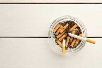 Glass ashtray with cigarette stubs on white wooden table, top view. Space for text