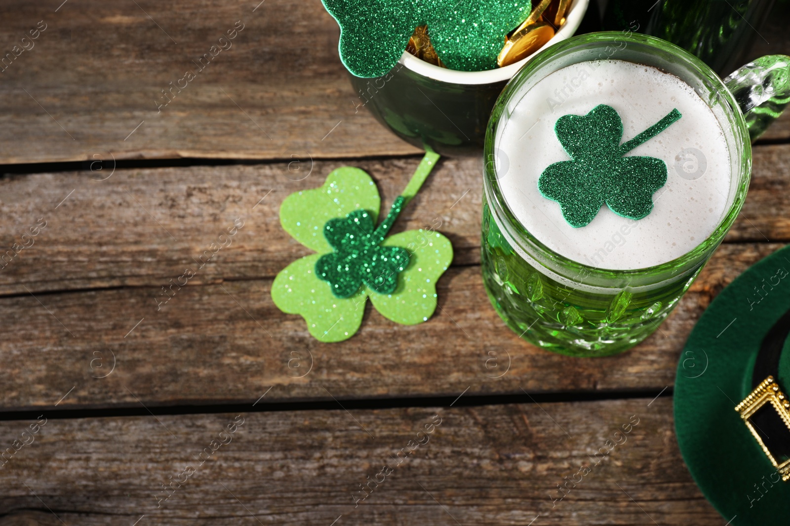 Photo of St. Patrick's day party. Green beer, leprechaun hat, pot of gold and decorative clover leaves on wooden table, above view. Space for text