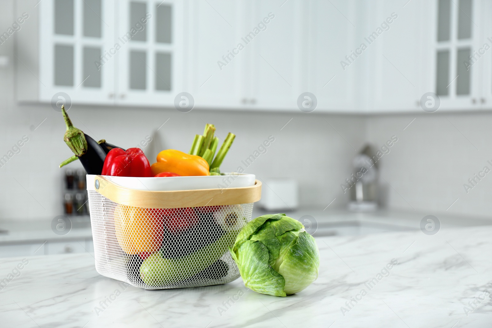 Photo of Different fresh vegetables in basket on white kitchen table. Space for text