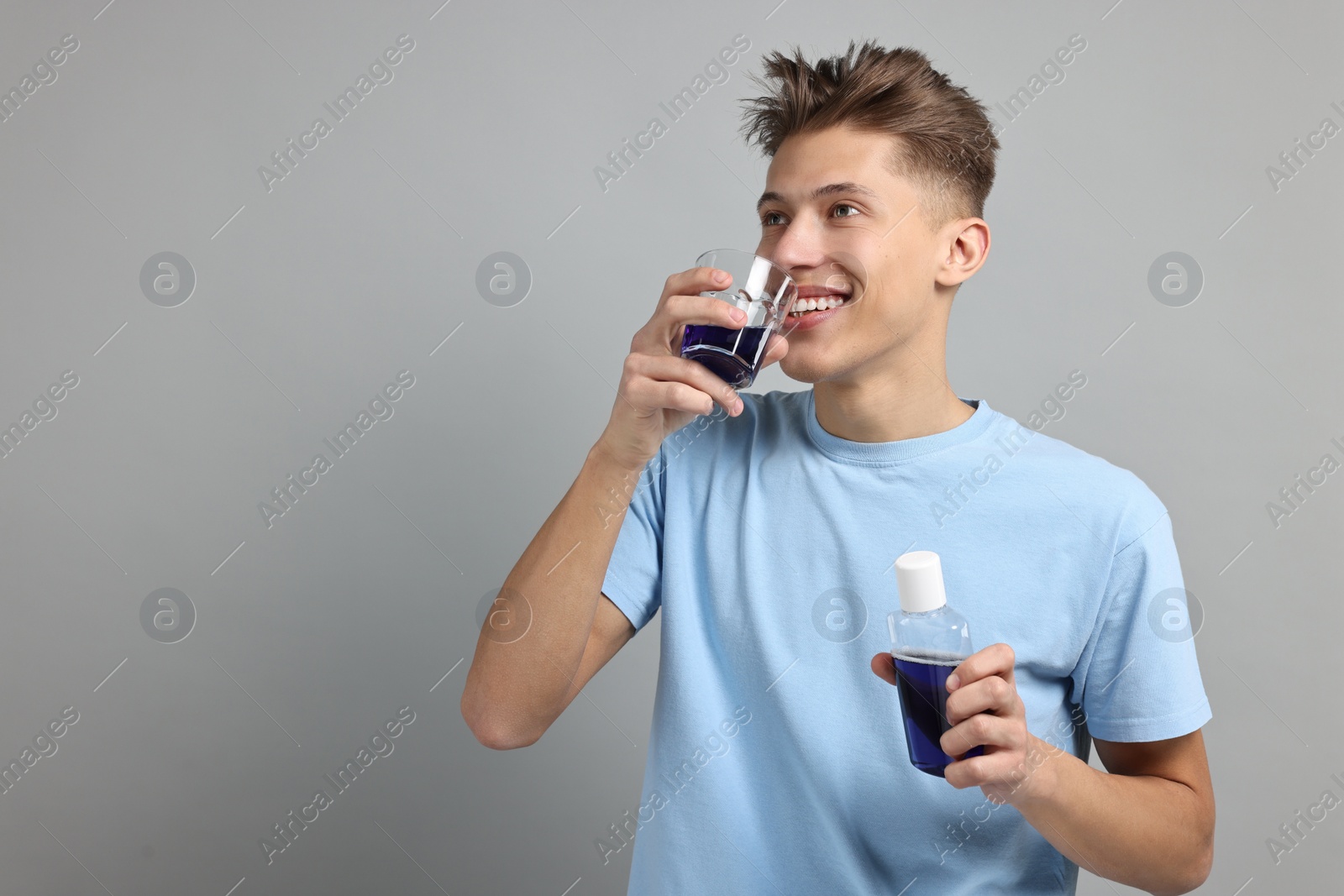 Photo of Young man using mouthwash on light grey background, space for text