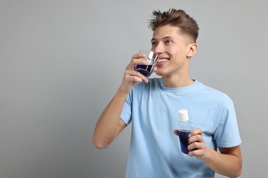 Photo of Young man using mouthwash on light grey background, space for text