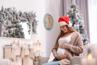 Photo of Young pregnant woman sitting on sofa in room decorated for Christmas