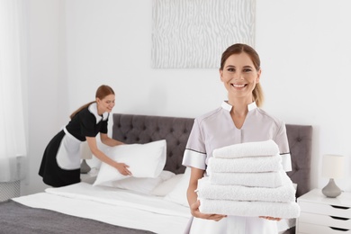 Photo of Professional chambermaid holding pile of clean towels in bedroom