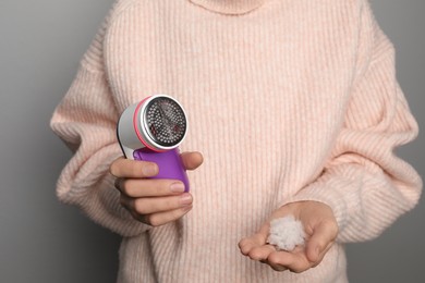 Photo of Woman in woolen sweater holding fabric shaver and lint on light grey background, closeup