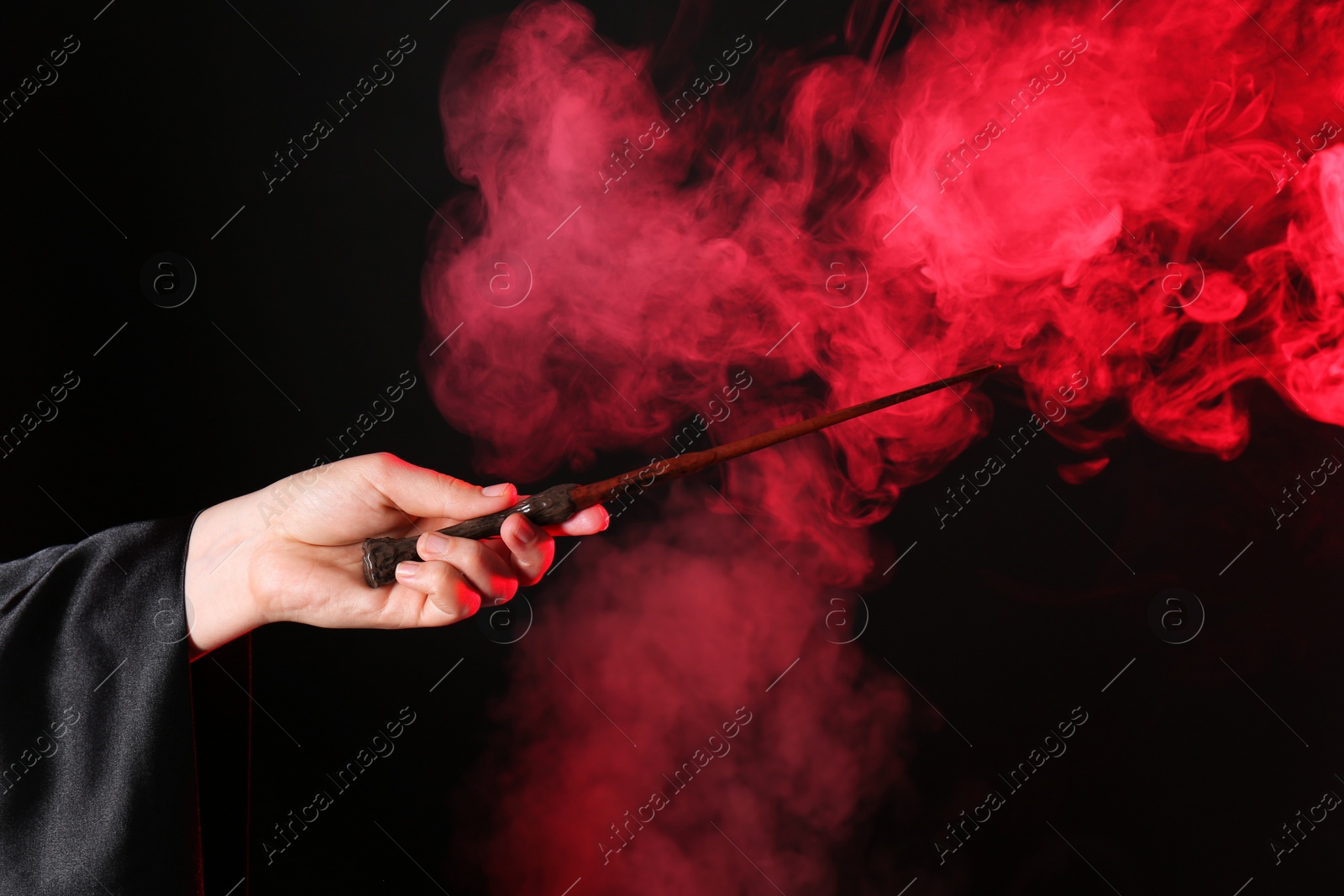 Photo of Magician holding wand in smoke on dark background, closeup