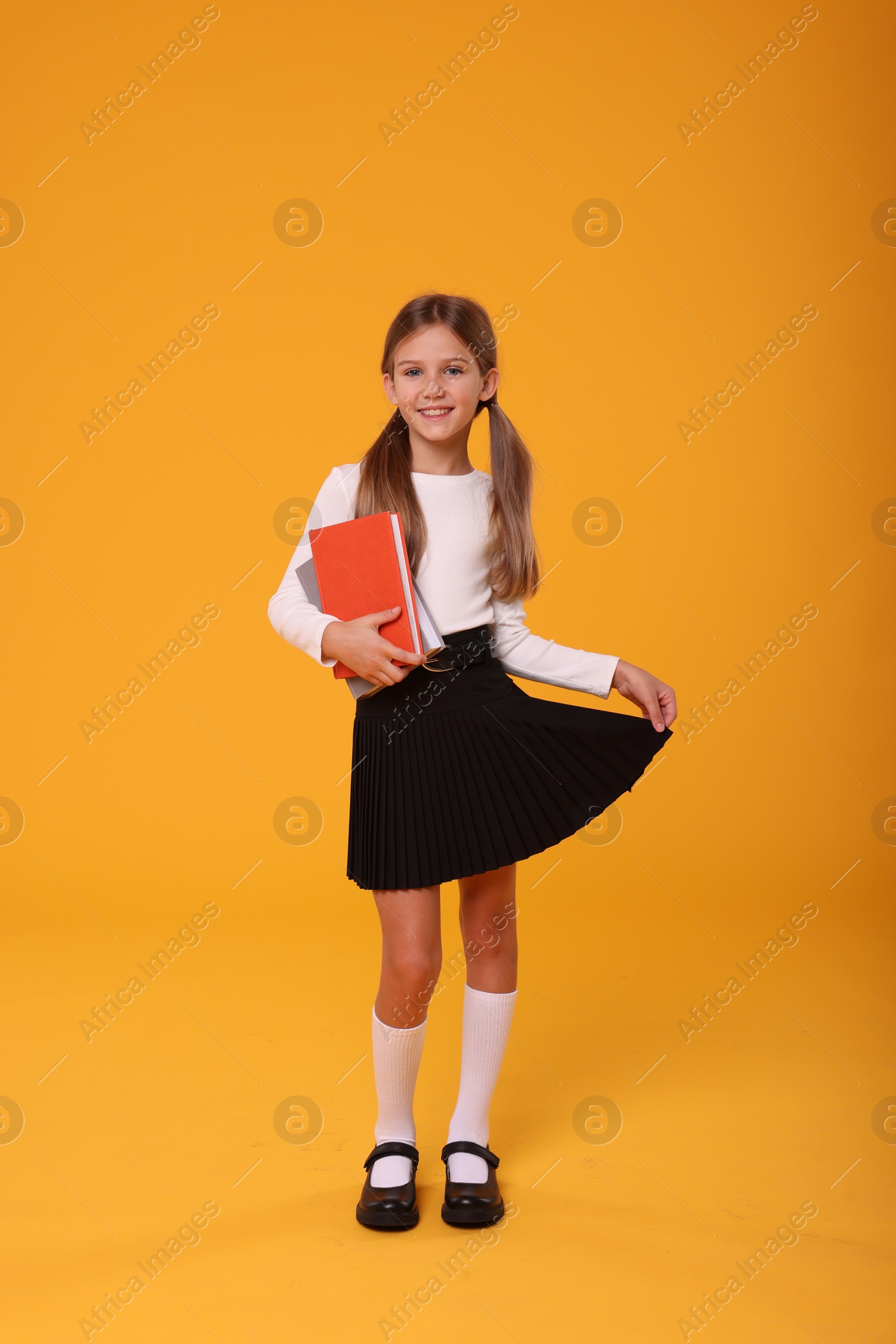 Photo of Happy schoolgirl with books on orange background